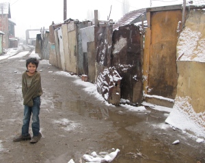 girl stands in a road of mud and snow by fences of old oil drums